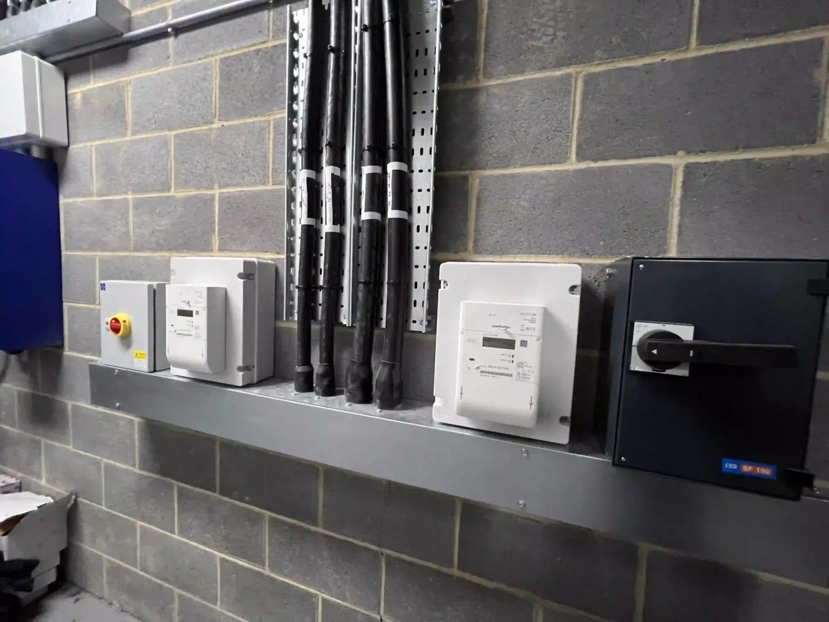 Commercial intake room: meters, isolators and cable tray on a blockwork wall