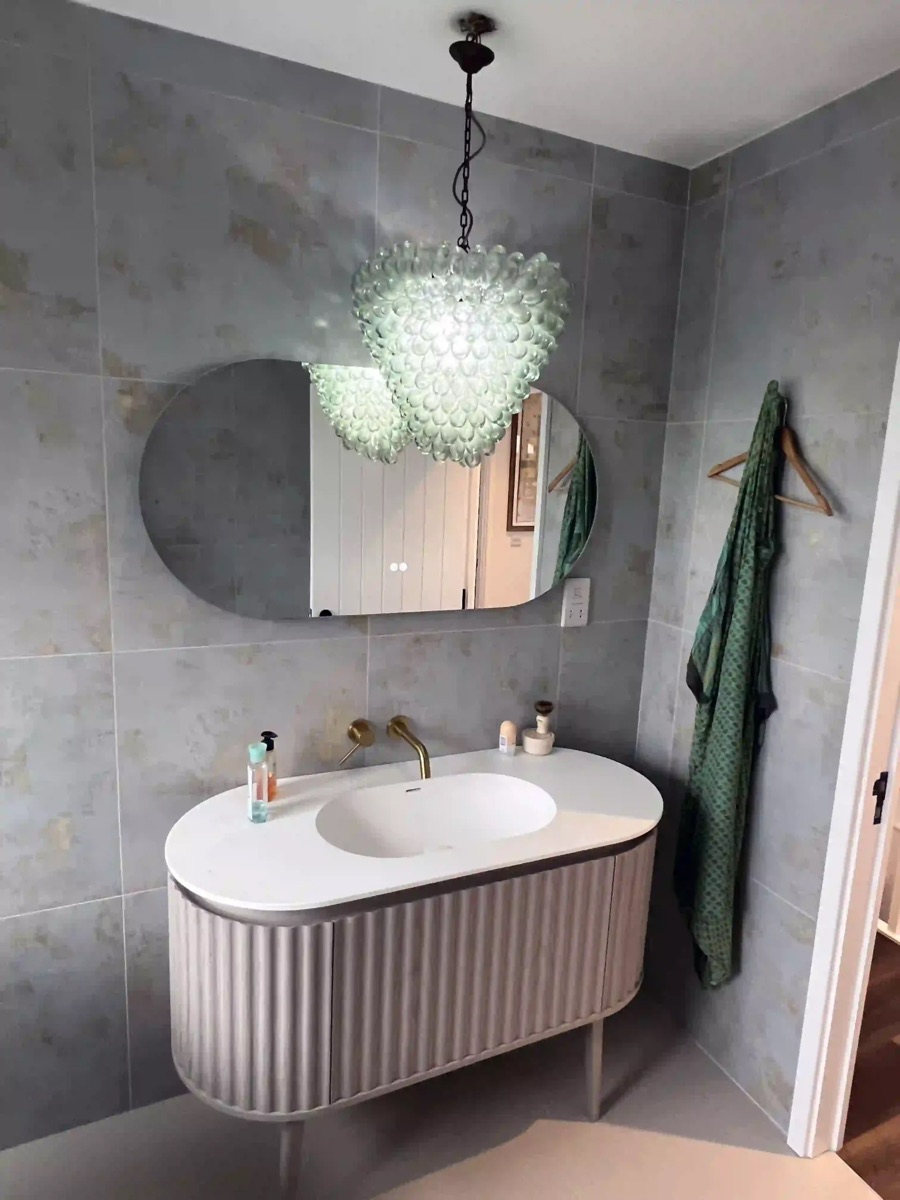 Bathroom with a glass pendant light above an oval mirror and vanity