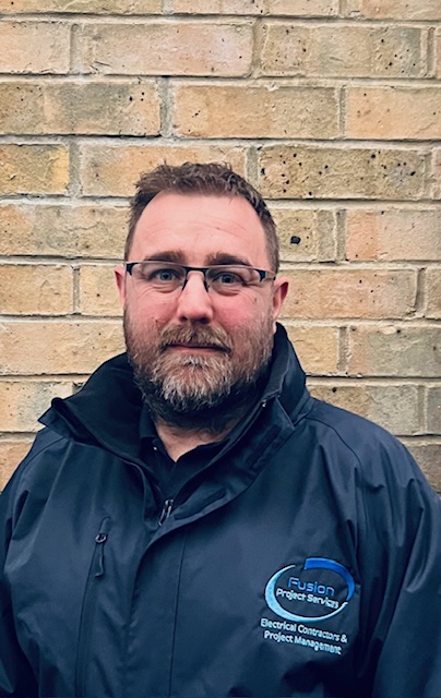 Iain Fudge in a navy Fusion Project Services jacket, standing against a brick wall